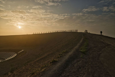 Road amidst field against sky during sunset