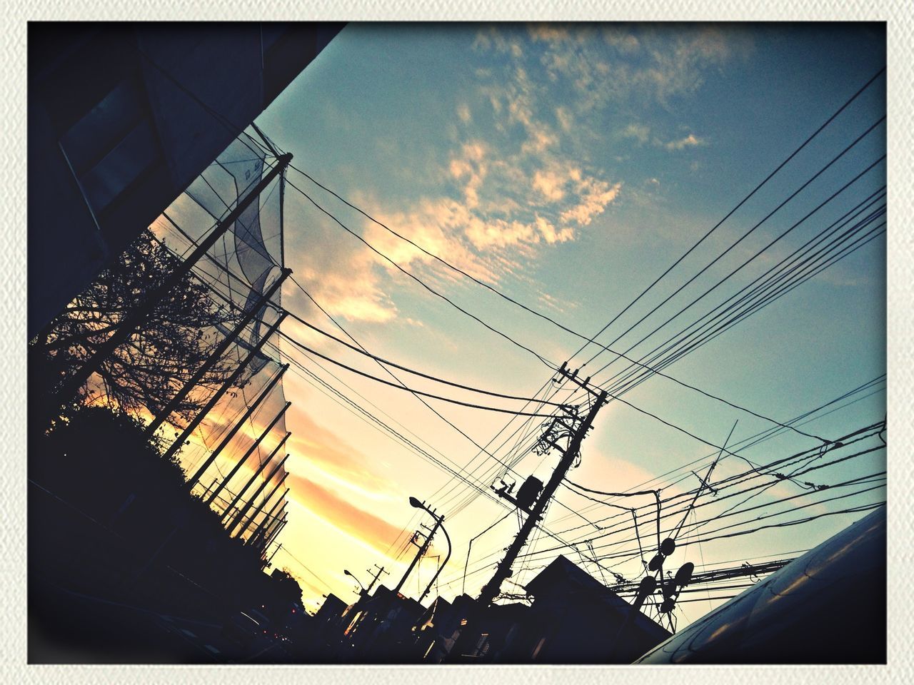 power line, electricity pylon, low angle view, power supply, electricity, silhouette, sky, cable, sunset, building exterior, connection, built structure, transfer print, technology, architecture, fuel and power generation, auto post production filter, power cable, cloud - sky, cloud