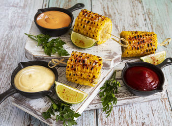 Grilled yellow corn with spices lime white red orange sauce portion top view