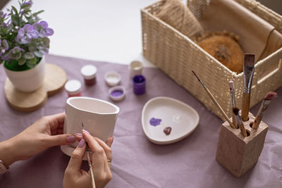 Womens hands paint a white flower ceramic pot