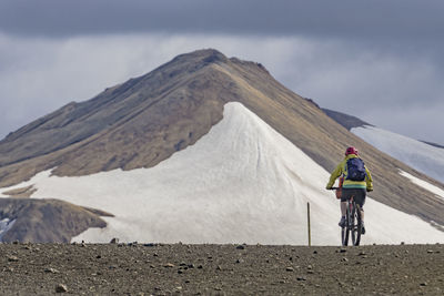 Man with bicycle on mountain against cloudy sky