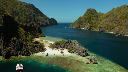 Tropical landscape bay with beach and clear blue water surrounded by cliffs, aerial drone. 