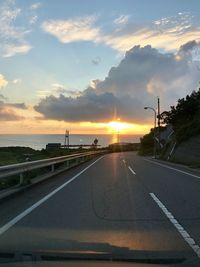 Road by sea against sky during sunset