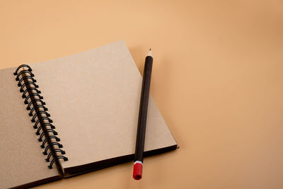Close-up of open spiral notebook with pencil on brown background