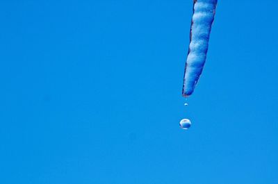 Water drops falling from melting icicle against clear blue sky