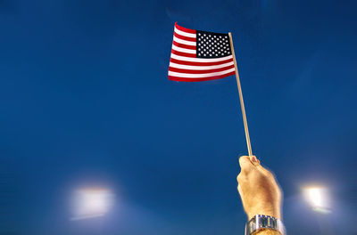Cropped hand holding american flag against sky at night