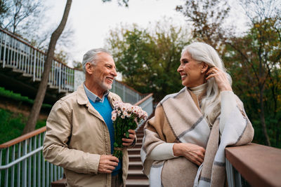 Smiling man holding bouquet standing with woman against trees