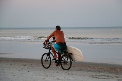 Man riding bicycle on shore at beach against clear sky