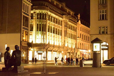 People on illuminated street amidst buildings at night