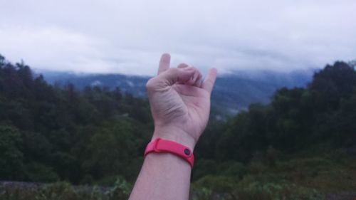 Midsection of person hand against trees against sky