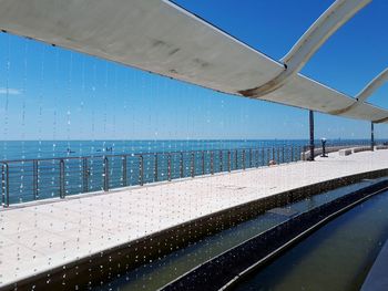 Swimming pool by sea against clear blue sky