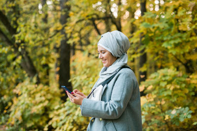 Young smiling woman using mobile phone in forest