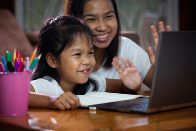 Smiling woman and girl waving over laptop