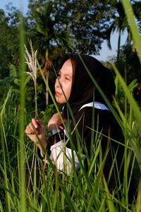 Young woman in hijab looking away amidst grass