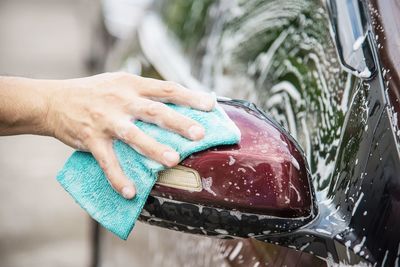 Cropped hands of man washing car side-view mirror