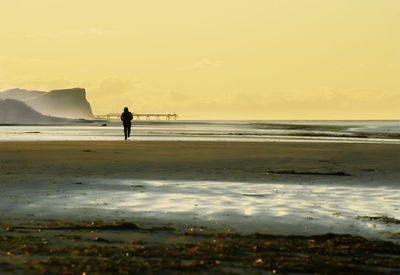 Silhouette man standing on beach against sky during sunset
