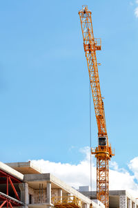 A tower crane jib leaps up over a construction site against a clear blue sky, vertical image.