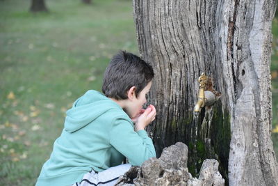 Side view of boy drinking water while crouching in park