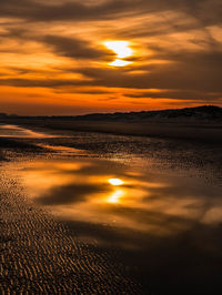 Colorful sunset with sun peeking through the overcast and sand ripples in the foreground at low tide