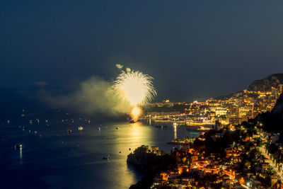 Firework display over illuminated city against sky at night