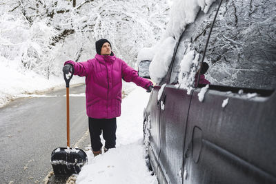 Thoughtful man with snow shovel standing by car on road