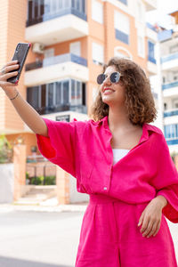 Young pretty curly haired woman taking selfie by smart phone in city. social media concept