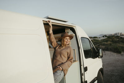 Happy young woman wearing hat standing in motor home
