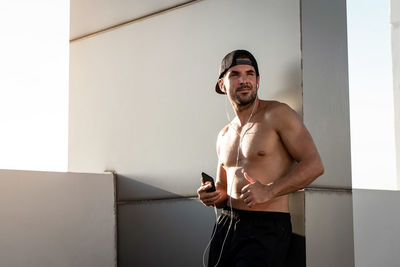 Smiling shirtless man standing by wall outdoors