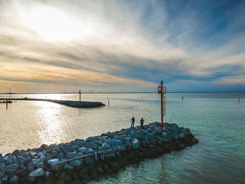 Friends standing on groyne against cloudy sky during sunset