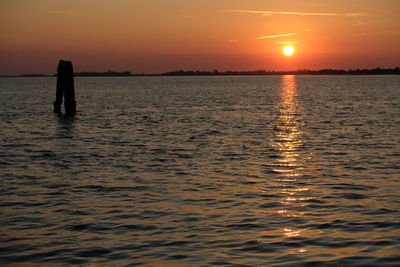 Silhouette person standing in sea against sky during sunset