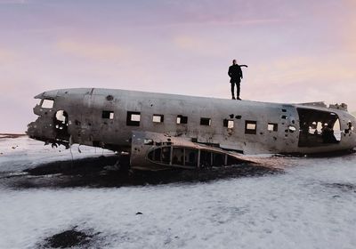 Man standing on abandoned airplane against sky during winter