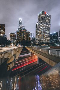 Illuminated bridge by buildings against sky in city