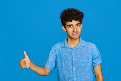Portrait of young woman with arms raised against blue background