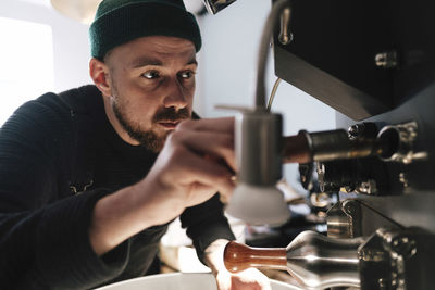 Coffee roaster wearing knit hat and operating machinery in factory
