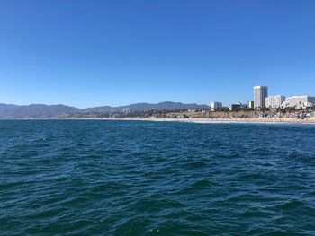 Scenic view of sea and buildings against clear blue sky