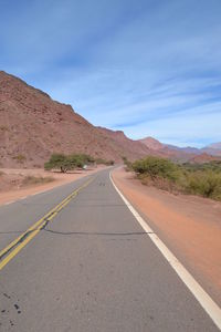 Empty road leading towards mountains against sky