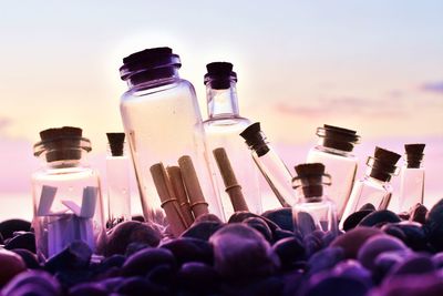 Close-up of letters in bottles at beach against sky during sunset