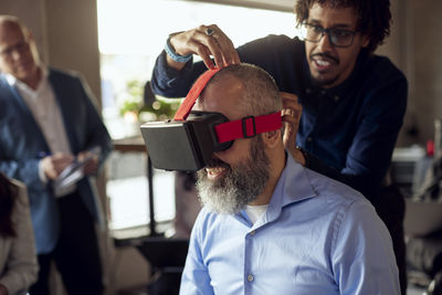 Businessman assisting male colleague in wearing vr simulator at creative office