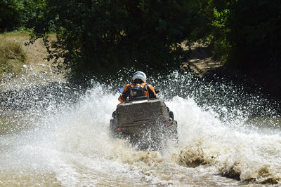 Rear view of person riding vehicle in river