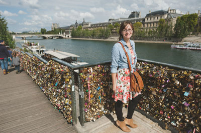 Portrait of woman standing by love locks on railing by river