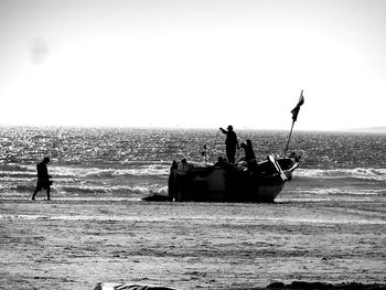 Silhouette people working on beach against sky