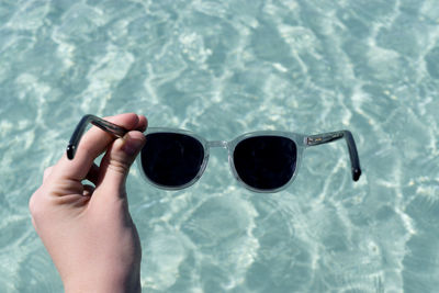 Cropped hand of woman holding sunglasses over swimming pool
