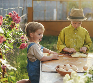 Brothers kneading dough on table in yard