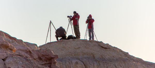 Low angle view of people photographing while standing on cliff against sky