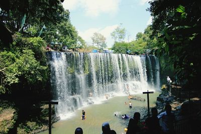 People by waterfall against trees