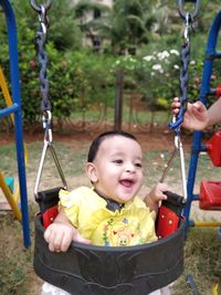 Cheerful baby girl on swing at playground