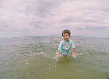 Boy playing in water against cloudy sky