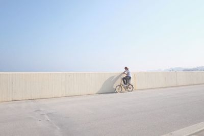 Man riding bicycle on bridge against clear sky