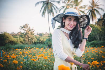 Young woman wearing hat while standing amidst flowers on field