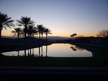 Silhouette palm trees by swimming pool against sky during sunset